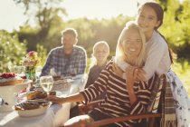 Portrait smiling affectionate mother and daughter hugging at sunny garden party patio table — Stock Photo