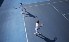 Young male doubles tennis players playing tennis on sunny blue tennis court — Stock Photo