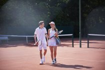 Tennis player couple walking, carrying tennis rackets on sunny clay tennis court — Stock Photo