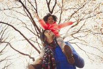 Padre llevando a la hija en hombros bajo el árbol en el parque de otoño - foto de stock