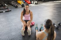 Mujeres jóvenes hablando y estirando las piernas en el gimnasio - foto de stock