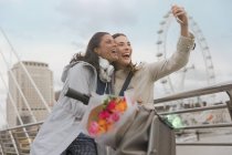Entusiasta, sorridente amiche donne prendere selfie con fotocamera telefono vicino Millennium Wheel, Londra, Regno Unito — Foto stock