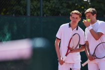 Young male tennis doubles players talking, strategizing — Stock Photo