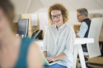 Portrait of woman using laptop and laughing, man working in background — Stock Photo