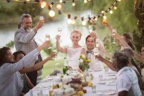 Junges Paar und seine Gäste stoßen bei Hochzeitsempfang im Garten mit Champagner an — Stockfoto