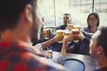 Amigos comemorando, brindando copo de cerveja na mesa de bar — Fotografia de Stock