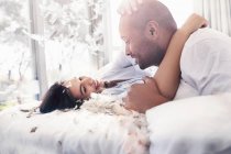 Piume di cuscino che cadono intorno giocoso, coppia affettuosa sul letto — Foto stock