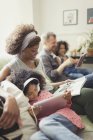 Familia joven multiétnica relajante, leyendo y usando tableta digital en el sofá - foto de stock