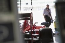 Менеджер изучает формулу один гоночный автомобиль в ремонтном гараже — стоковое фото