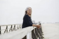 Портрет впевнена старша жінка спирається на пляжні рейки — стокове фото