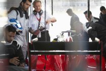 Manager and formula one driver watching pit crew working on race car in repair garage — Stock Photo
