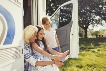 Mãe e filhas usando tablet digital fora ensolarado motor casa — Fotografia de Stock