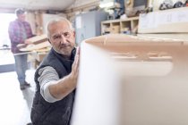 Male carpenter examining, touching wood boat in workshop — Stock Photo