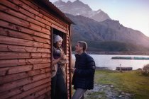 Young couple drinking coffee at lakeside cabin doorway — Stock Photo
