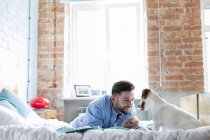 Hombre jugando con Jack Russell Terrier perro en la cama - foto de stock