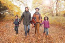 Портрет улыбающейся молодой семьи, держащейся за руки и идущей по тропинке в осеннем парке — стоковое фото