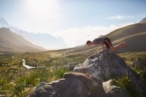Молодой человек балансирует на руках на скале в солнечной, отдаленной долине — стоковое фото