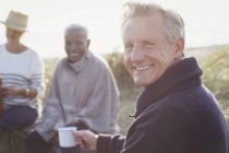 Портрет улыбающийся пожилой мужчина пьет кофе с друзьями на солнечном пляже — стоковое фото