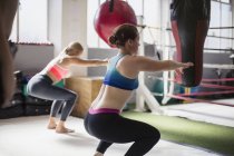 Junge Frauen beim Kniebeugen neben dem Boxring im Fitnessstudio — Stockfoto