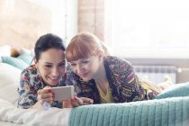 Women using cell phone laying on bed — Stock Photo