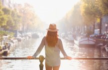 Mulher usando chapéu olhando para a vista do canal ensolarado outono, Amsterdã — Fotografia de Stock