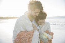 Молода пара, загорнута в ковдру на пляжі — стокове фото