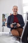 Улыбающийся портрет, уверенный в себе мужчина-фотограф с цифровой камерой в офисе — стоковое фото