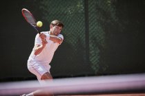 Giovane tennista di sesso maschile che gioca a tennis, colpendo la palla sul campo da tennis soleggiato — Foto stock