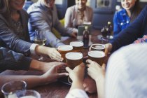 Friends reaching for beer glasses on bar table — Stock Photo