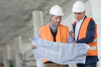 Male engineers examining underground blueprints at construction site — Stock Photo