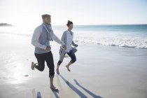 Молода пара тримається за руки і бігає на пляжі — стокове фото