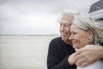 Casal sênior afetuoso abraçando e olhando para longe na praia — Fotografia de Stock
