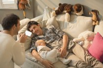 Чоловіки гей-батьки і дитина син відпочиває на дивані у вітальні — стокове фото