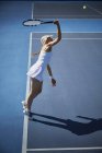 Молода тенісистка грає в теніс, досягаючи з тенісною ракеткою на сонячно-блакитному тенісному корті — стокове фото