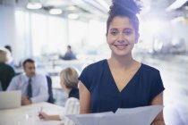 Porträt lächelnde, selbstbewusste junge Geschäftsfrau mit Papierkram im Büro — Stockfoto