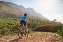 Junge Mountainbikerin auf sonnigem, abgelegenem Feldweg — Stockfoto