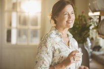 Усміхнена зріла жінка п'є вино на кухні — стокове фото