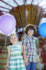 Retrato de niño y niña sosteniendo globos en parque de atracciones - foto de stock