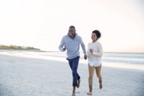 Пара держащихся за руки и бегущих по пляжу — стоковое фото