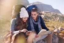 Young couple with backpacks hiking, resting and checking map and smart phone — Stock Photo