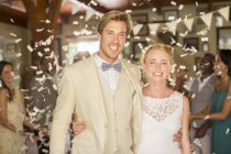 Retrato de la joven pareja sonriente de pie en confeti caída durante la recepción de la boda - foto de stock