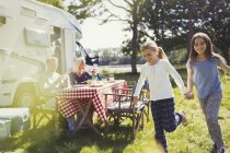 Happy sisters holding hands and running around sunny motor home — Stock Photo