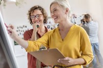 Smiling female design professionals with clipboard meeting at flipchart in office — Stock Photo