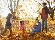 Joven familia jugando en las hojas de otoño en el parque soleado - foto de stock