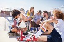Friends in roller skates hanging out listening to music at sunny skate park — Stock Photo