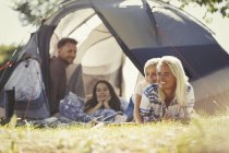 Família sorridente relaxante fora da tenda ensolarada no acampamento — Fotografia de Stock