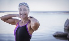 Портрет улыбающейся женщины, плавающей на открытой воде, регулирующей купальник в океане — стоковое фото