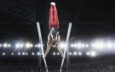 Male gymnast performing upside-down handstand on parallel bars in arena — Stock Photo