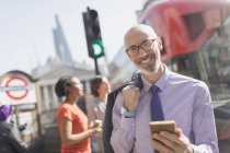 Retrato sonriente hombre de negocios con teléfono celular en la soleada calle urbana, Londres, Reino Unido - foto de stock