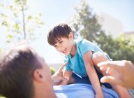 Figlio ridente sdraiato sulla cima del padre sul patio soleggiato — Foto stock